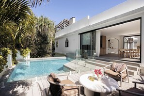 A modern outdoor pool area with a glass balustrade, wooden deck, and outdoor furniture.