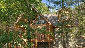 Une cabane en bois avec des fondations en pierre, un balcon et un escalier menant à l’entrée.