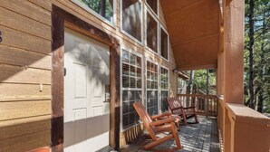 Une véranda en bois avec des fauteuils à bascule, une porte blanche et un paillasson sur lequel est écrit « Bonjour ».