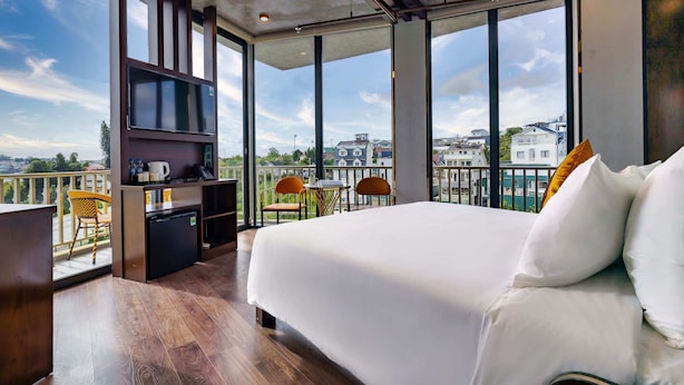 A modern hotel room with a large bed, a small kitchenette, and a balcony with chairs and a table. - Phuc Hai Hotel Da Lat (Lang Biang - Da Lat)