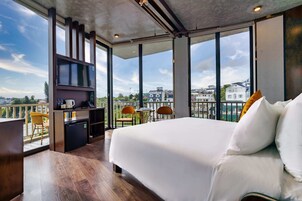 Quarto de hotel moderno com uma cama grande, uma kitchenette pequena e uma varanda com cadeiras e mesa.