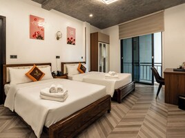 Quarto de hotel com duas camas, uma escrivaninha, uma cadeira e varanda com vista.