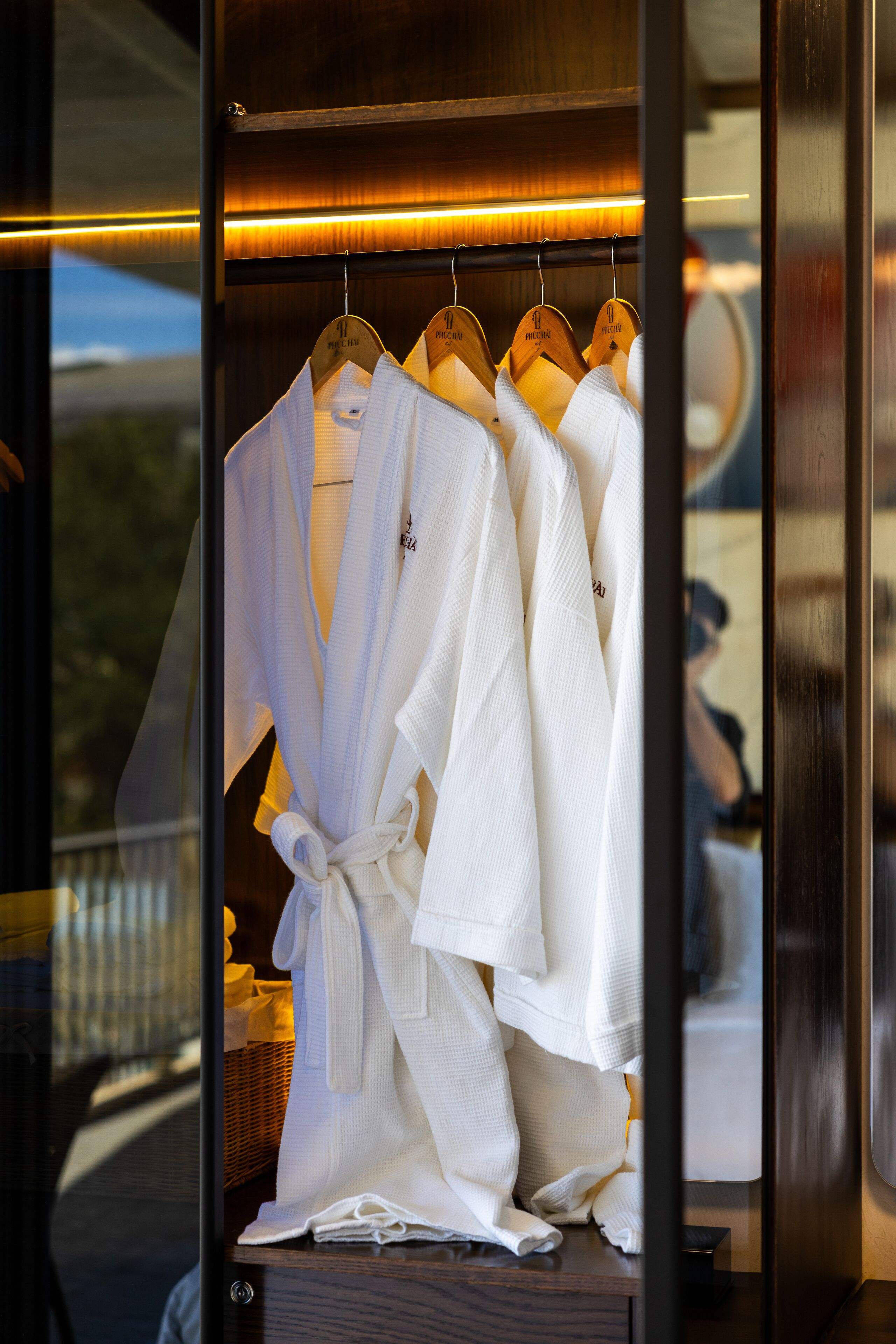 A wooden wardrobe with white robes hanging on hangers.