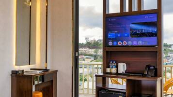 Habitación de hotel con una cama grande, un televisor sobre un soporte de madera, un refrigerador pequeño y un balcón con vistas.