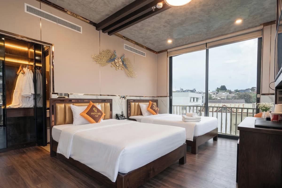 Quarto de hotel com duas camas, uma escrivaninha e uma janela grande com vista para a cidade.
