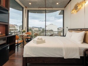Un dormitorio con cama, televisión, una mesita con sillas y vistas a la ciudad.