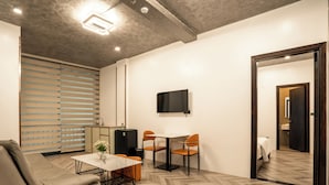 A modern living room with a sofa, a table, and chairs, a flat-screen TV mounted on the wall, and a door leading to a bathroom. - Phuc Hai Hotel Da Lat (Lang Biang - Da Lat)