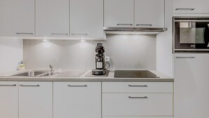 Una cocina moderna con armarios blancos, horno empotrado y cafetera.