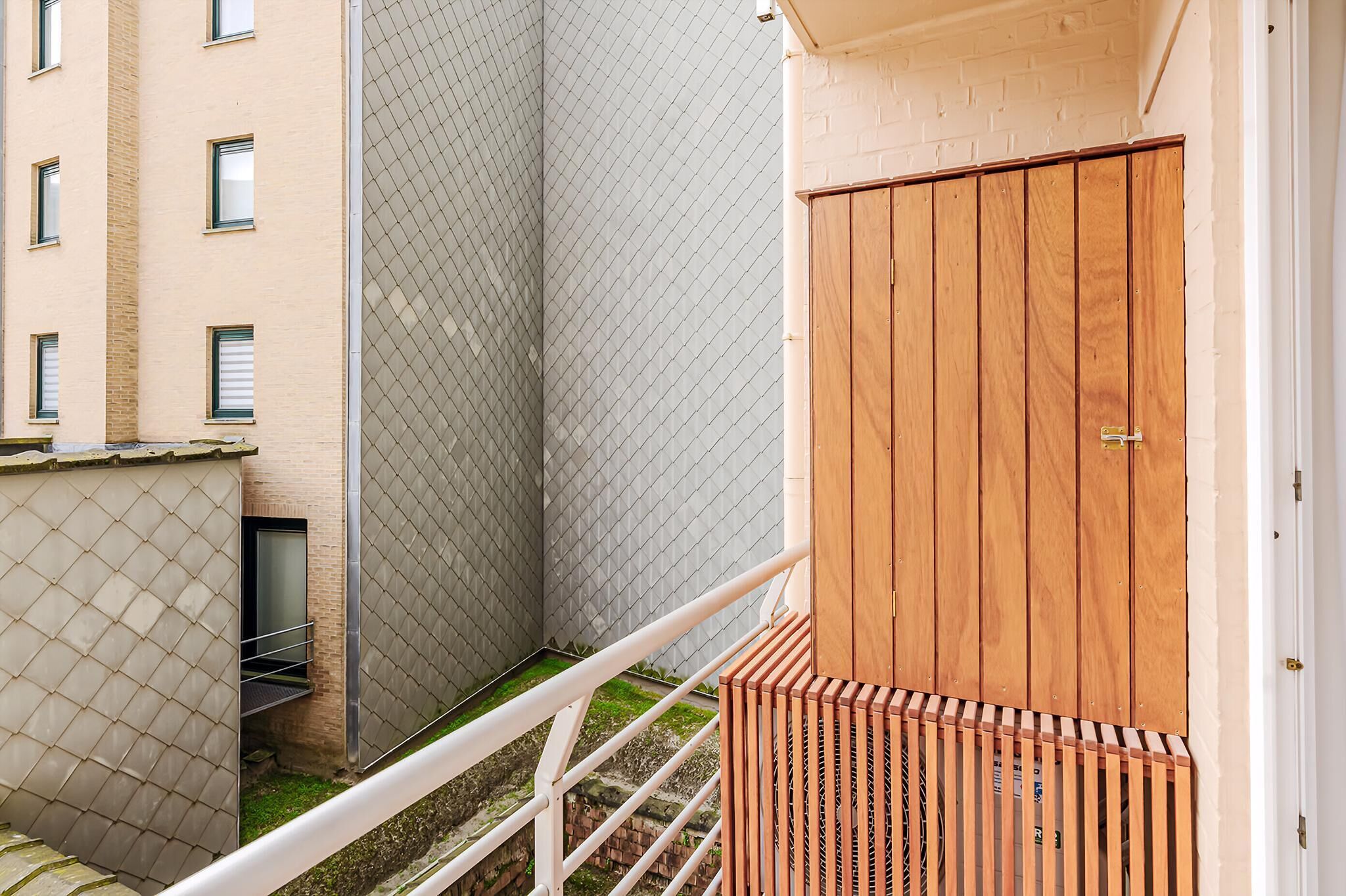 Un couloir étroit, avec une clôture en métal, une porte en bois et une rambarde blanche.