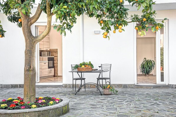 Ein Innenhof mit Steinboden, einem Tisch mit Stühlen, einem Orangenbaum und einem Blumentopf.