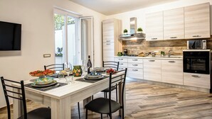 Une cuisine moderne avec des meubles en bois, un four encastré et un coin repas avec une table dressée pour quatre personnes.