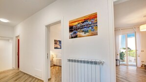 Un couloir avec un radiateur, une porte donnant sur une pièce et un tableau représentant un paysage côtier.