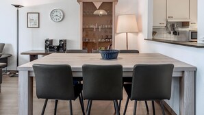 Ein moderner Essbereich mit einem Holztisch, schwarzen Stühlen, einem blauen Korb, einer Uhr und einer Lampe.