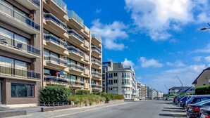 Ein mehrstöckiges Wohngebäude mit Balkonen, einem Parkplatz und blauem Himmel.