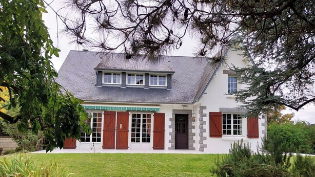 A two-story house with a sloped roof, a front porch, and a stone pathway leading to the entrance.