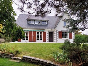 Ein zweistöckiges Haus mit geneigtem Dach, einer Veranda und einem Kiesweg, der zum Eingang führt.