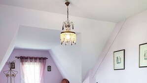 A bedroom with two beds, a chandelier, a window with curtains, and a wooden floor.