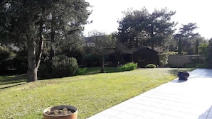 A well-maintained garden with a paved walkway, a small shed, and a variety of trees and shrubs.