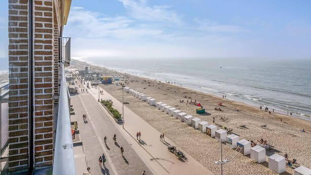 Ein Strand mit gepflastertem Weg, Strandsonnenschirmen und Menschen, die die Gegend genießen.