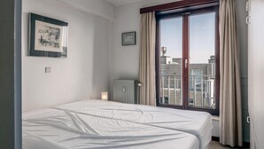 Ein Hotelzimmer mit einem großen Bett, einem Heizkörper, einem gerahmten Bild und einem Vorhangfenster.