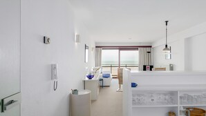 Ein modernes Hotelzimmer mit großem Fenster, einer weißen Minibar, einem Schreibtisch mit Lampe und Meerblick.