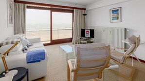 Ein Hotelzimmer mit Sofa, Sessel, Fernseher, Tisch und Meerblick.