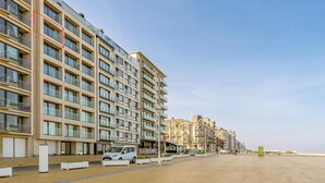 Un edificio moderno de varios pisos con balcones, un sendero pavimentado y un automóvil estacionado.