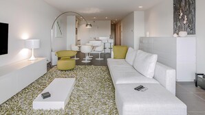 Un salon moderne avec un canapé blanc, des fauteuils jaunes, une table basse blanche et un grand tableau accroché au mur.