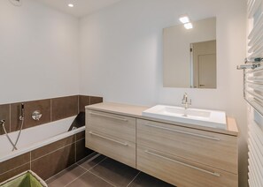 Une salle de bain moderne avec une baignoire, un lavabo et un meuble-lavabo doté de tiroirs.
