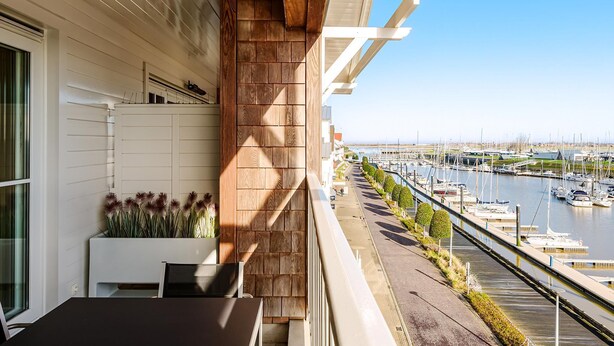Un balcon donnant sur un port de plaisance, avec une balustrade blanche et un pot de fleurs.
