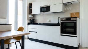 A modern kitchen with white cabinets, a black countertop, a microwave, an oven, and a dining area with a wooden table and a chair. - Via Casilina 161 in Rome (Rome)