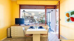 A dining area with a table, chairs, a TV, and a window with a view of trees and a balcony. - il nido sul Mare by Interhome (Cervo)