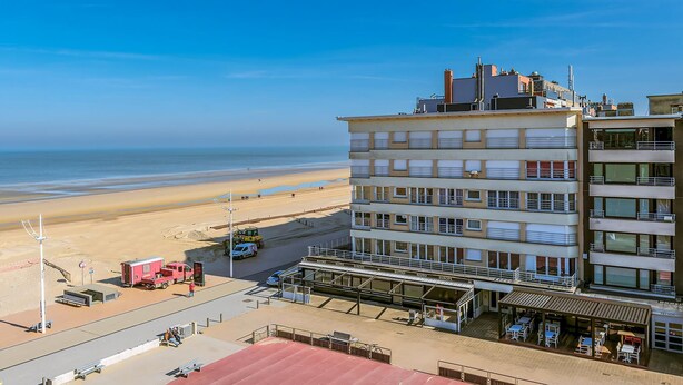 A multi-story hotel with a beach view, outdoor seating area, and a red vehicle parked on the beach. - 1 bedroom accommodation in Sint Idesbald (Sint Idesbald)