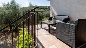 Une terrasse extérieure aménagée avec des meubles en osier, une rambarde en métal et une vue sur la verdure environnante.