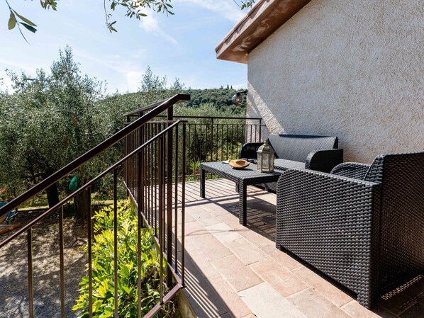 An outdoor patio with wicker furniture, a metal railing, and a view of the surrounding greenery.