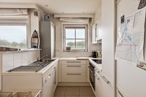 A compact kitchen with white cabinets, a built-in oven, and a window with a view of trees.