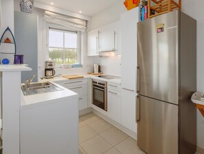A modern kitchen with white cabinets, stainless steel appliances, a built-in oven, and a large refrigerator.