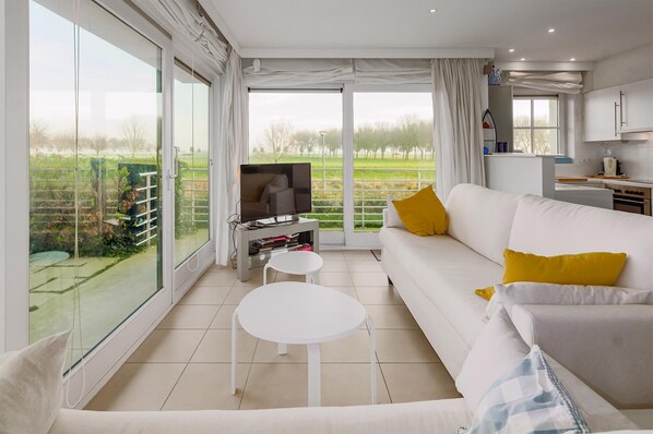 A modern living room with a white sofa, yellow pillows, a flat-screen TV, and a small white table.