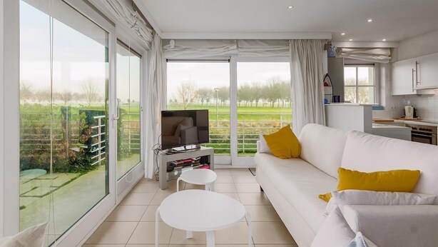 A modern living room with a white sofa, yellow pillows, a flat-screen TV, and a small white table. - Zonnehaven II G 0002+G93 (NIEUWPOORT)
