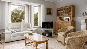 A living room with a white sofa, a wooden coffee table, wicker chairs, a TV stand, and a cabinet with glass doors.