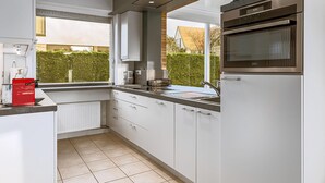 A modern kitchen with white cabinets, a stainless steel oven, and a window overlooking a garden.