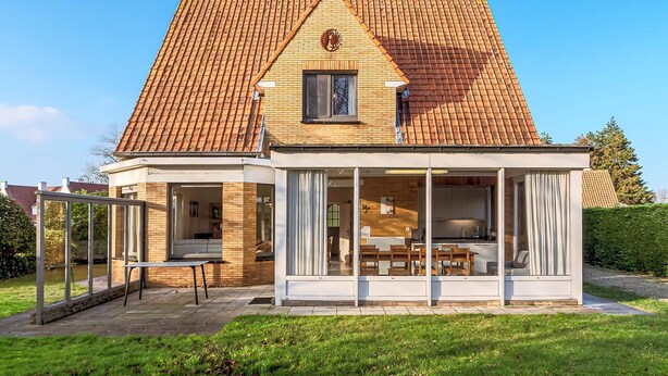 A house with a tiled roof, a covered patio with a table and chairs, and a garden.