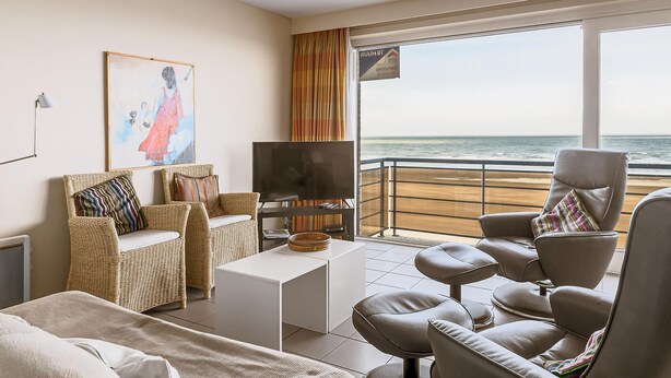 A modern living room with a large window overlooking the sea, furnished with a sofa, chairs, and a coffee table.