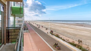 A beachfront promenade with a clear view of the ocean, a pedestrian path, and a building with a green awning.