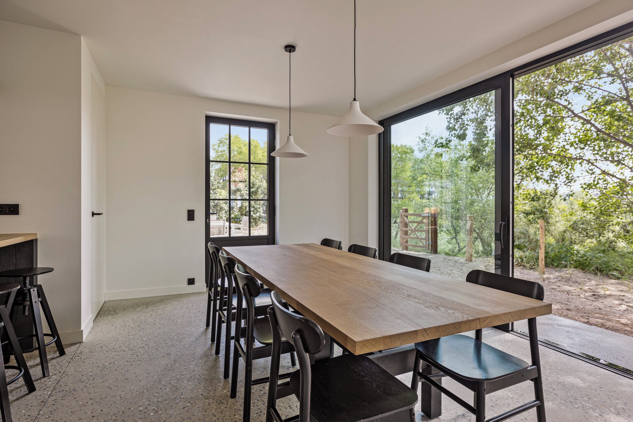 Un espace de salle à manger moderne avec une longue table en bois, des chaises noires et des luminaires suspendus.