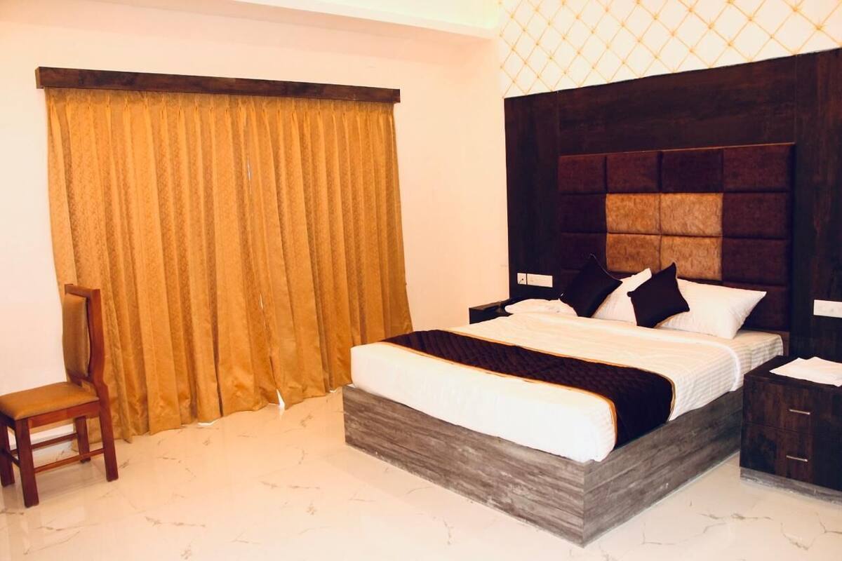 Ein Hotelzimmer mit einem großen Bett, einem Nachttisch aus Holz, einem Sessel und einem Fenster mit Vorhängen.