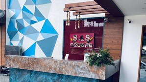 A reception desk with a geometric wall design, a wooden reception area, and a plant on the counter. - SAS SQUARE (Tiruchirappalli)