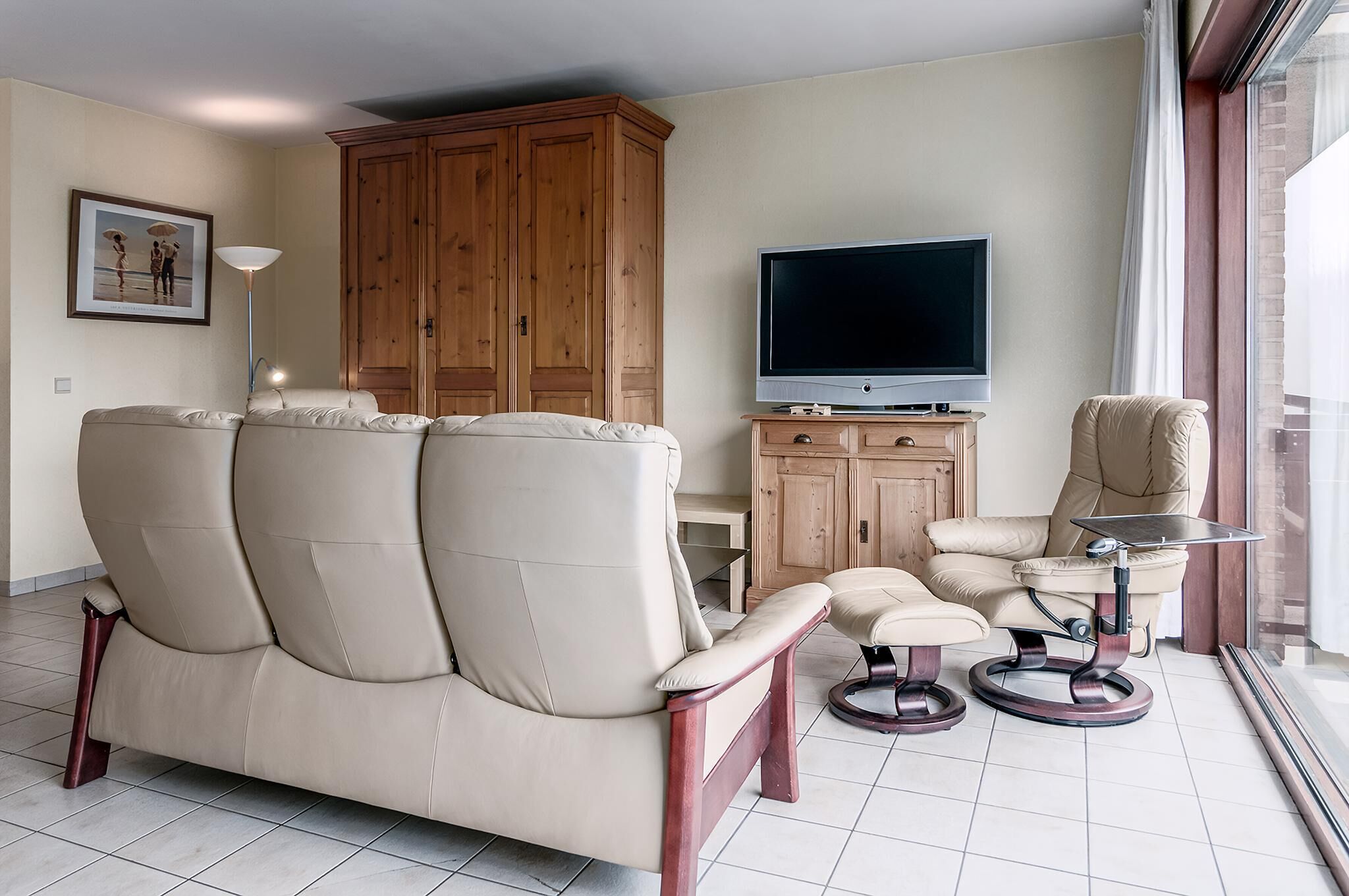 Ein Wohnzimmer mit beiger Couch, einem kleinen Tisch, einem Fernseher und einem Holzschrank.