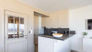 A modern kitchen with a white door, a large island with a bowl, and a flat-screen TV mounted on the wall.