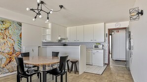 Een moderne keuken met witte kasten, een centraal eiland en een eethoek met een glazen tafel en stoelen.